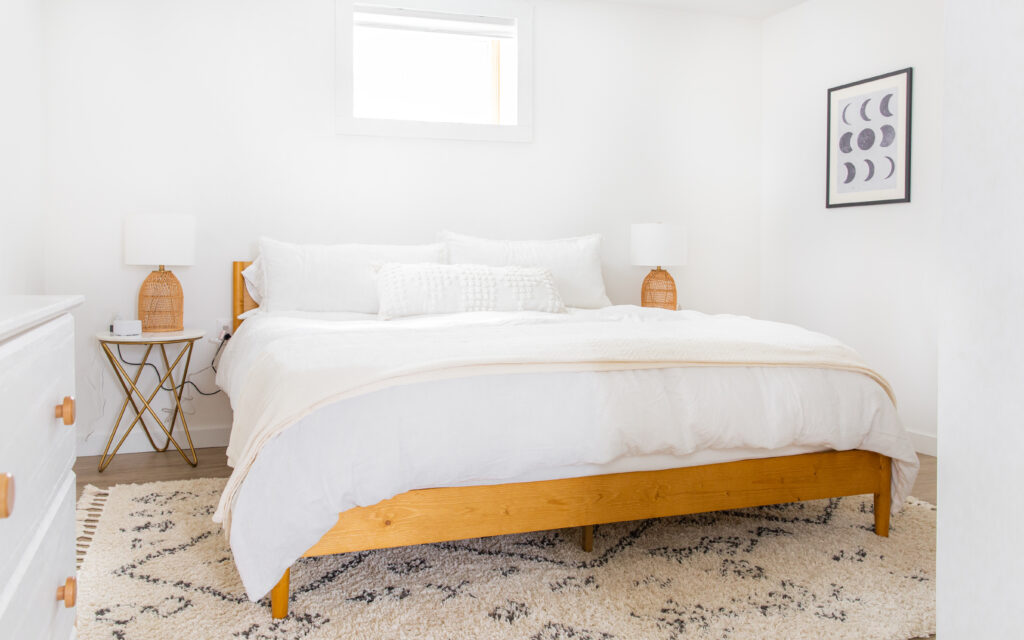 neutral bedroom with king bed, white sheets and wood accents