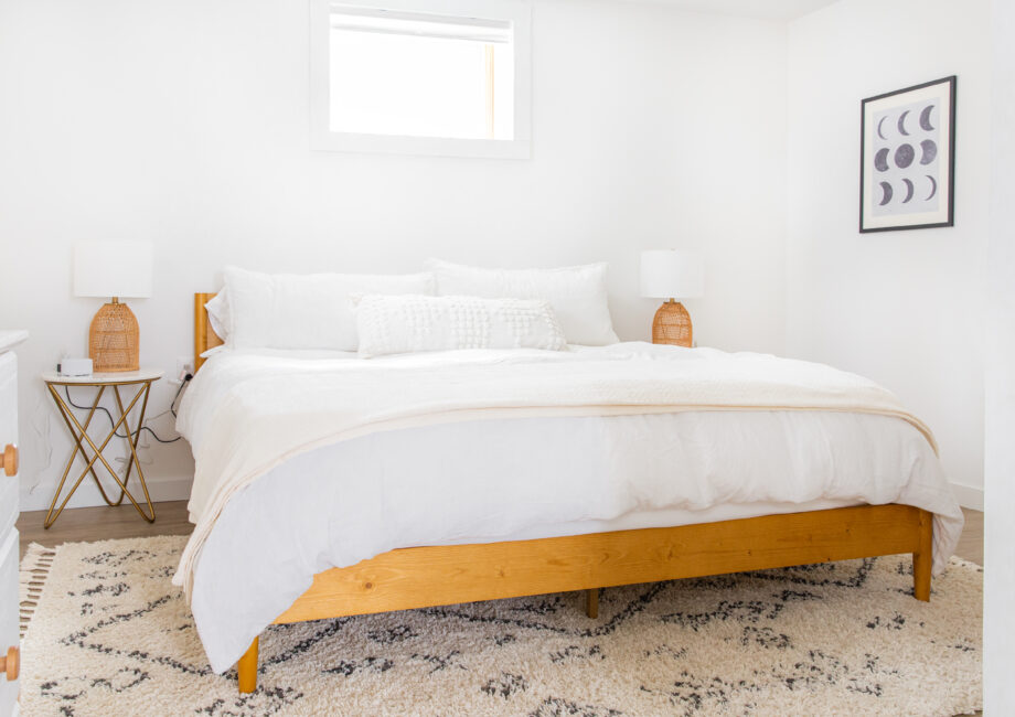 neutral bedroom with king bed, white sheets and wood accents